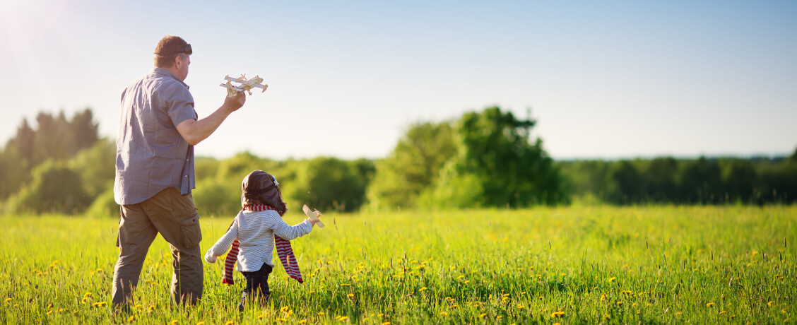 Father and young son playing with toy aeroplane in field 